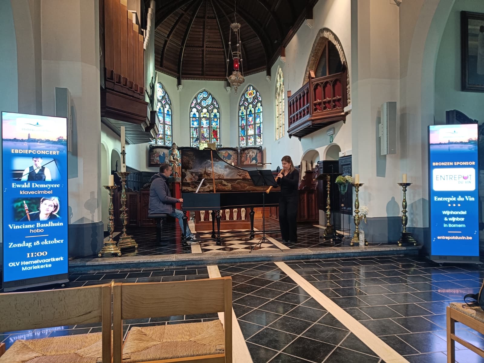 Twee LED-wanden naast de musici in de OLV Hemelvaartkerk Mariekerke, concert van 18 oktober 2026